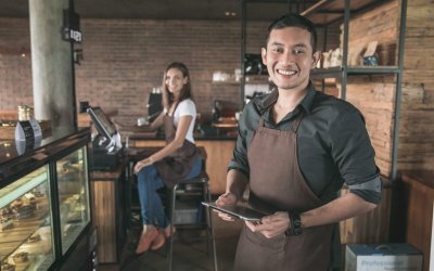 cafe owner at his coffee shop using tablet pc. his partner sitting in a background